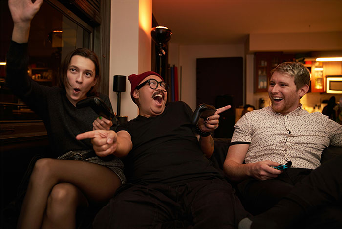 Three friends laughing and holding game controllers in a living room, capturing a moment before a knife slipped accident.