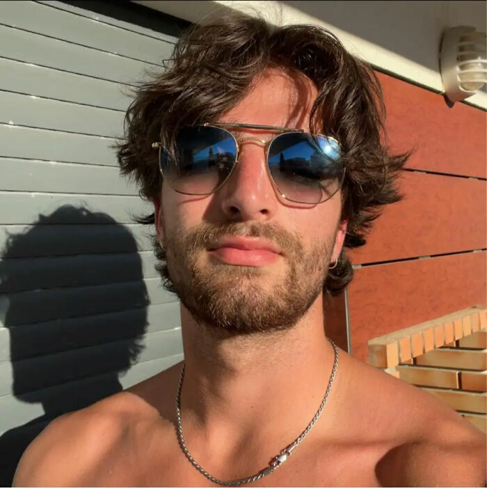 Young man wearing sunglasses and a chain necklace posing outdoors with sunlight and shadows in the background. Young man wearing sunglasses and a chain necklace posing outdoors with sunlight and shadows in the background.