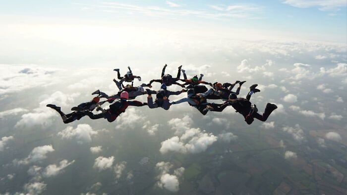 Group of skydivers in formation above clouds during a high-altitude jump capturing the thrill of a 15,500-ft fall. Group of skydivers in formation above clouds during a high-altitude jump capturing the thrill of a 15,500-ft fall.