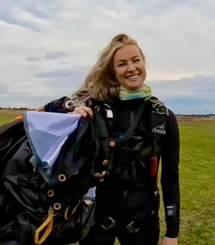 Woman in skydiving gear smiling outdoors after a 15,500-ft jump following a breakup, inspiring many online. Woman in skydiving gear smiling outdoors after a 15,500-ft jump following a breakup, inspiring many online.