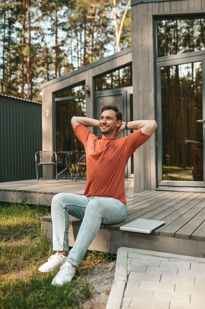 Young man sitting outside modern house, looking relaxed and happy, reflecting on smartest kids in their class stories.