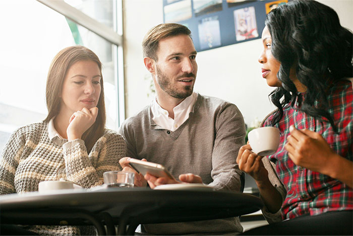 Three people using social cheat codes in a casual café setting, engaged in conversation and observing each other.