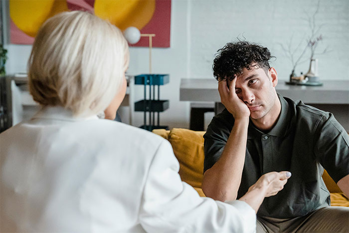 Man sitting on sofa looking thoughtful while woman talks to him, illustrating social cheat codes through observation.