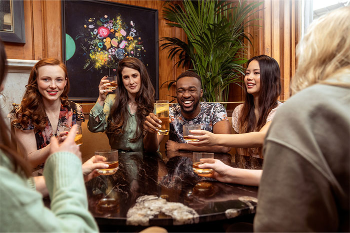 Group of friends happily socializing and enjoying drinks together, showcasing social cheat codes from observing others.