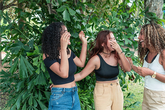 Three young women laughing together outdoors, illustrating social cheat codes learned by quietly observing others.