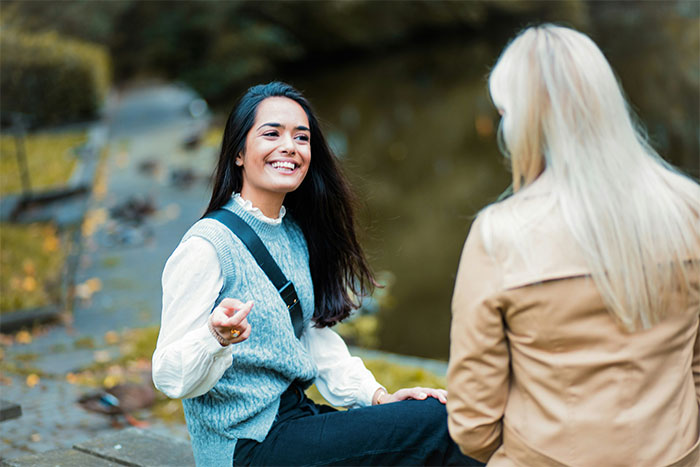 Two women engaging in a friendly conversation outdoors, exemplifying social cheat codes learned through quiet observation.