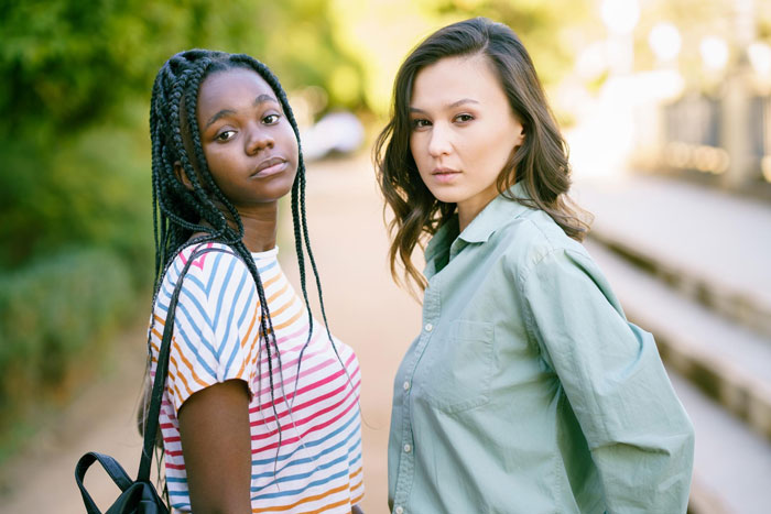 Two teenage girls, one black and one Asian, standing outdoors with serious expressions, highlighting a tense moment.