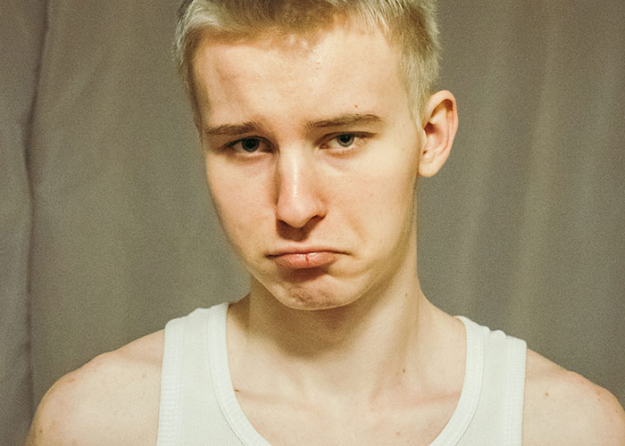 Sad young man in a white tank top showing disappointment and vulnerability, representing a gay son facing family rejection.