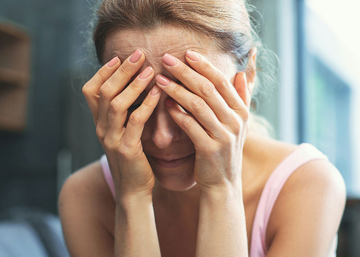 Woman covering her face with hands, showing distress and emotional struggle related to family conflict over son's identity.