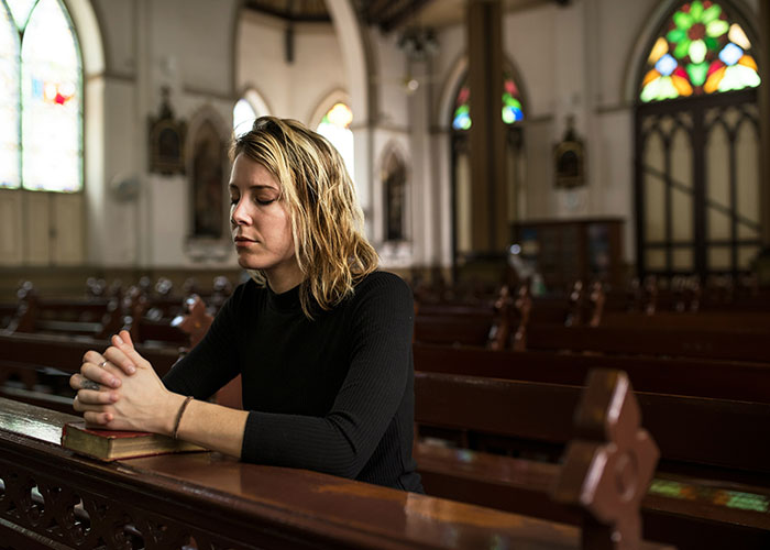 Woman in black sitting alone inside a church, reflecting on family struggles related to dad standing by gay son.