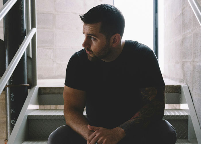 Man with tattooed arm sitting on stairs, looking contemplative, representing dad stands by gay son support theme.