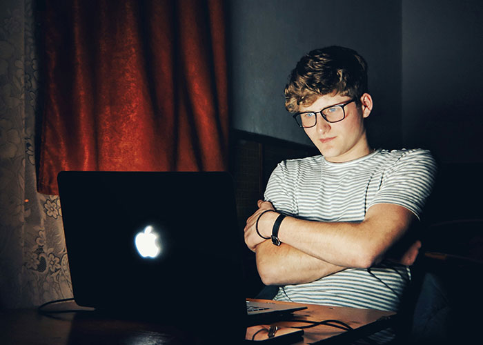 Young man with glasses sitting at a table looking at a laptop, representing dad stands by gay son support.