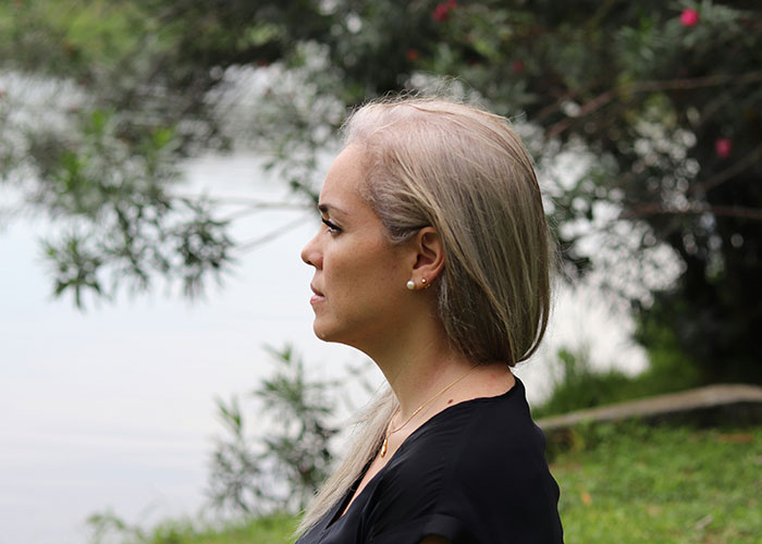 Woman with long blonde hair in profile sitting outside near a lake, reflecting on her son&rsquo;s coming out and family support.