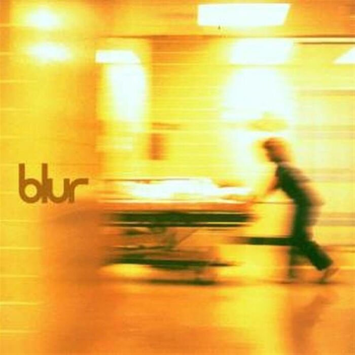 Blur album cover with blurred figure pushing a hospital stretcher in a bright, yellow-toned hallway, evoking eerie space fear themes.