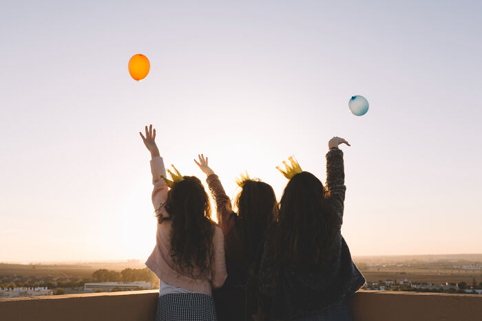 Three people wearing crowns outdoors at sunset, reaching toward floating balloons, illustrating space is scarier than we think.