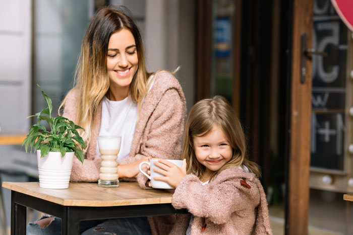 Woman on a 12-month hiatus from work smiling with child at caf&eacute; table, expecting more money than &pound;150 weekly allowance.