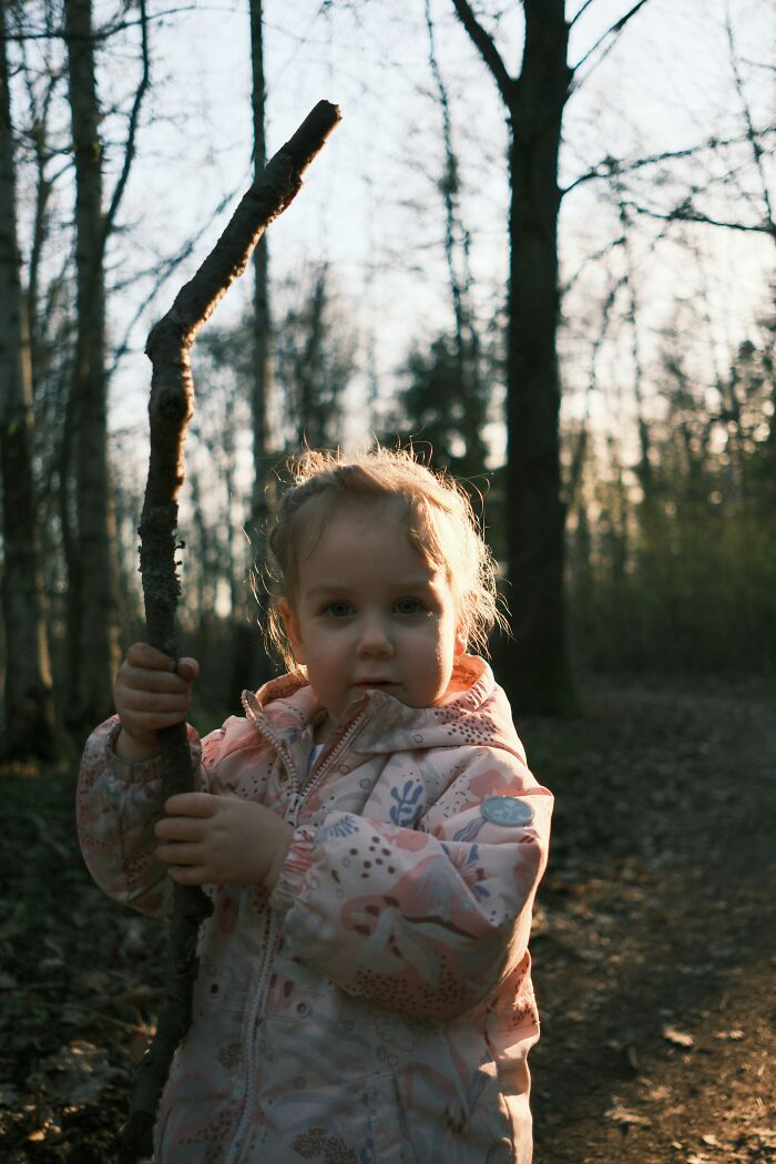 Young girl in a forest holding a stick, evoking creepy and terrifying experiences parents had with kids' imaginary friends.