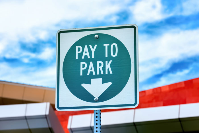 Pay to park sign posted outside a building under a partly cloudy blue sky with focus on illegal parking warnings.