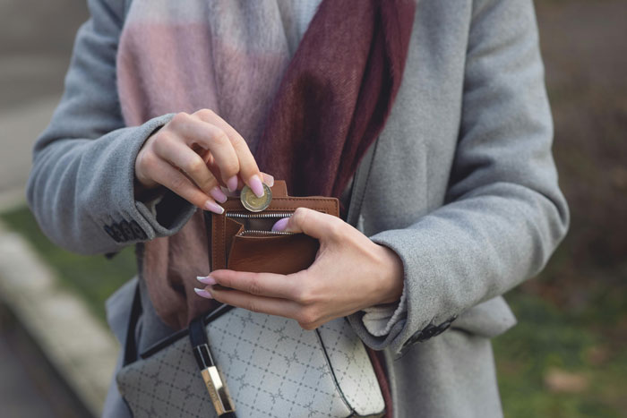 Woman holding wallet outdoors, putting a coin inside while wearing a gray coat and scarf, illustrating karma at grocery store. Woman holding wallet outdoors, putting a coin inside while wearing a gray coat and scarf, illustrating karma at grocery store.