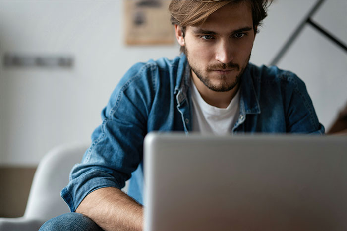 Man looking upset and focused on a laptop, reflecting emotions of resentment and humiliation in a tense moment.