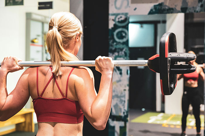 Woman lifting barbell in gym, showing toned back and arms, focused on strength training workout session.