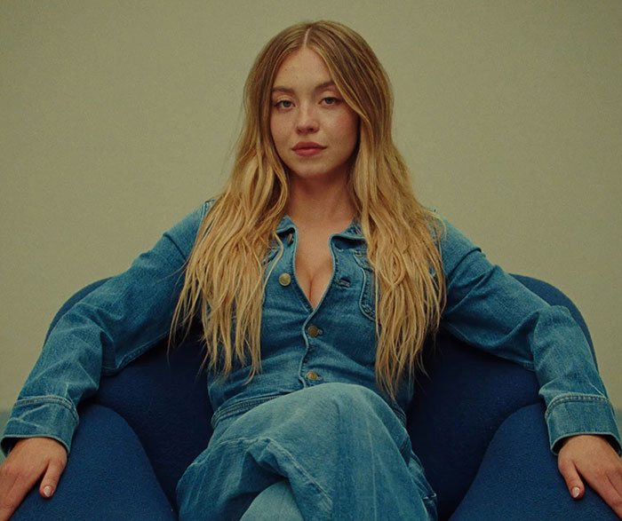 Sydney Sweeney seated in a denim outfit, breaking social media silence after Genes ad amid online trolling.