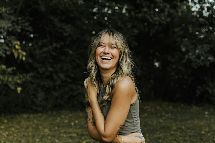 Woman laughing outdoors with casual clothes, illustrating favorite ways to avoid babysitting shared online by 30 people.