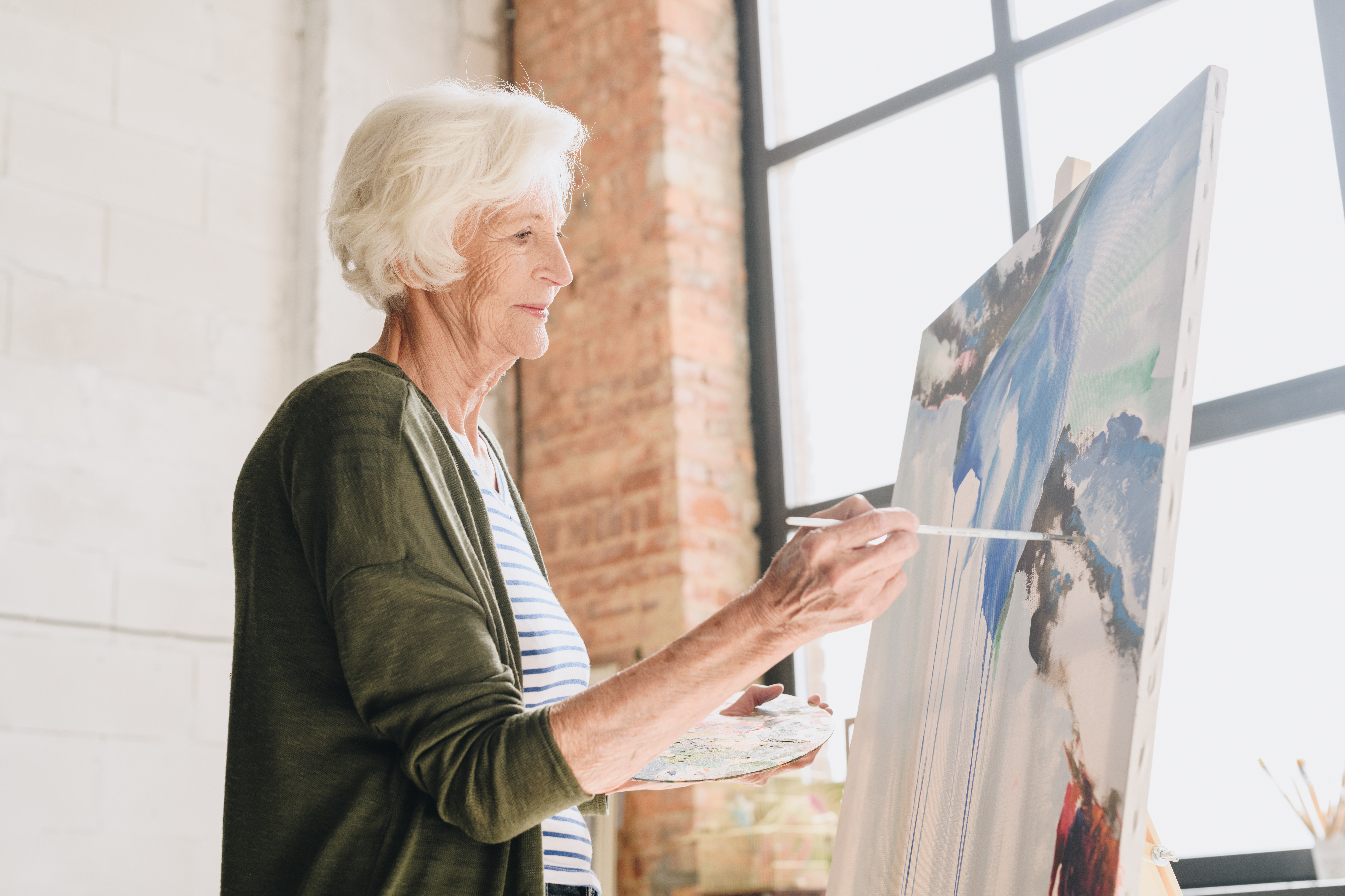 Elderly woman painting on canvas in bright studio, expressing creativity and unexpected artistic inspiration.