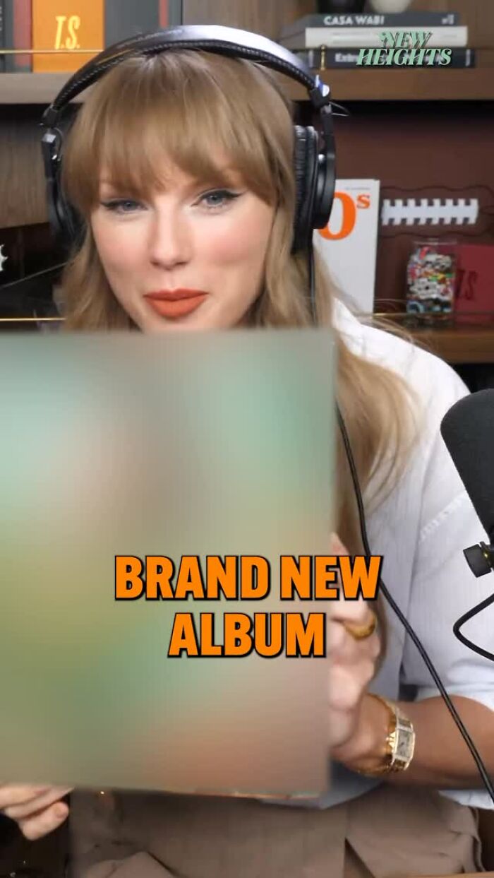 Taylor Swift wearing headphones, revealing her brand new album in a cozy studio setting with books in the background.