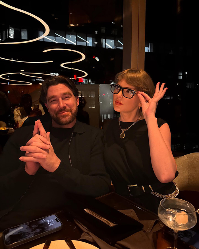 Taylor Swift wearing glasses next to Travis Kelce in a dimly lit restaurant, fans spot hidden engraving on engagement ring. Taylor Swift wearing glasses next to Travis Kelce in a dimly lit restaurant, fans spot hidden engraving on engagement ring.