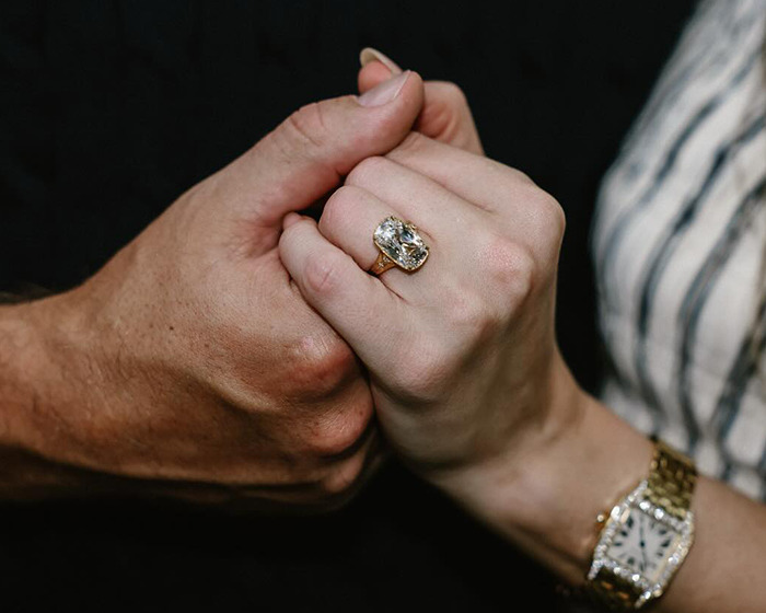 Close-up of hands showing an engagement ring with a large diamond and fans spotting Travis Kelce's hidden engraving. Close-up of hands showing an engagement ring with a large diamond and fans spotting Travis Kelce's hidden engraving.