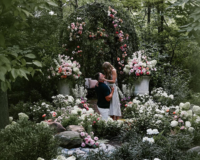 Couple embraces in a lush garden filled with blooming flowers, symbolizing romance and engagement ring moments. Couple embraces in a lush garden filled with blooming flowers, symbolizing romance and engagement ring moments.