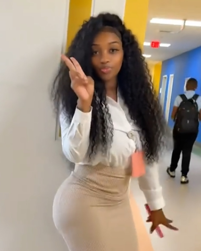 Teacher posing in a hallway, sparking viral debate for showing off curves in back-to-school outfit with confident gesture.