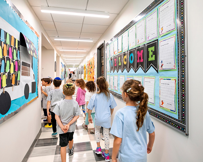 Elementary students walking in a school hallway decorated with colorful back-to-school decorations and welcome signs.