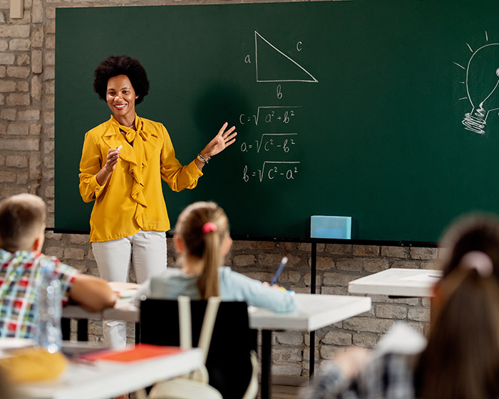 Teacher in yellow blouse teaching math with triangle formulas on chalkboard in classroom with attentive students.