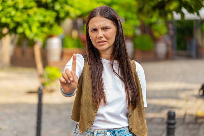 Woman outdoors with long hair, raising index finger in a gesture of rejection or refusal, symbolizing teen stepson conflict. - 21