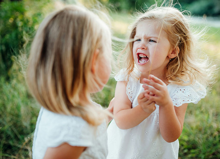 Two young girls outdoors, one visibly upset, depicting a family fallout and conflict between half-sisters. Two young girls outdoors, one visibly upset, depicting a family fallout and conflict between half-sisters.