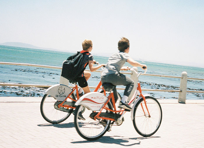 Two children riding bicycles by the sea, illustrating person tells half-sister they ran away causing family fallout. Two children riding bicycles by the sea, illustrating person tells half-sister they ran away causing family fallout.