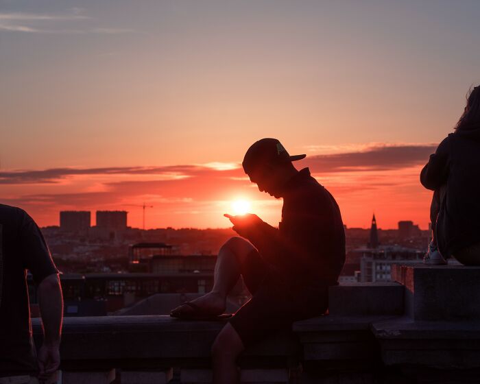 Silhouetted young man using phone at sunset on rooftop, reflecting on what happened to the smartest kids in class.