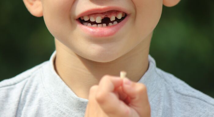 Close-up of a child smiling with a missing tooth, holding the lost tooth, illustrating disturbing facts related to teeth.
