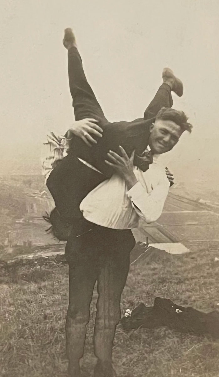 Vintage candid glimpse of two men playfully lifting each other outdoors, capturing a rare moment from the past.