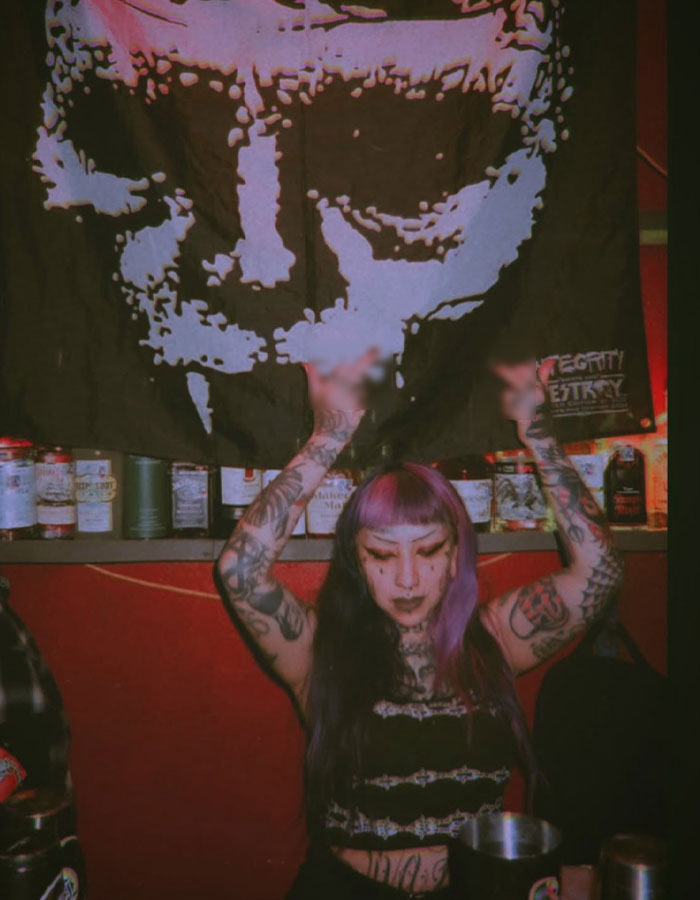 Person with tattoos and purple hair raising hands in a dimly lit room, illustrating sickening details about school shooting plans. - 3