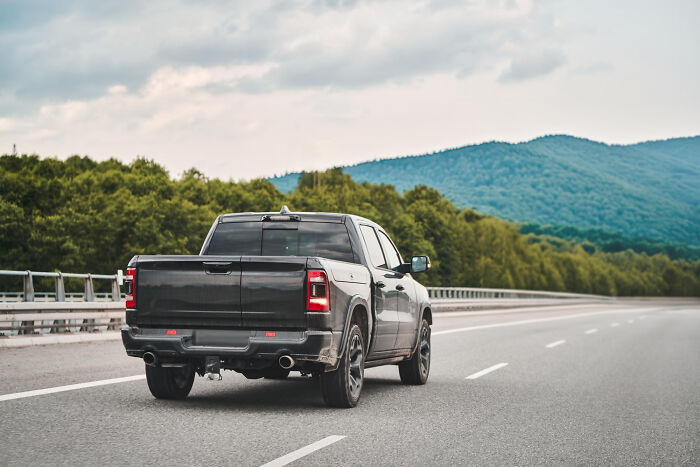 Black pickup truck driving on empty highway with green trees and mountains, evoking childhood memories that felt sweet back then.