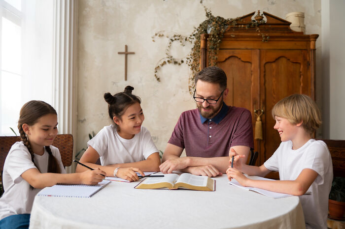 A man teaching three children at a table, evoking childhood memories that felt sweet but became unsettling in retrospect.