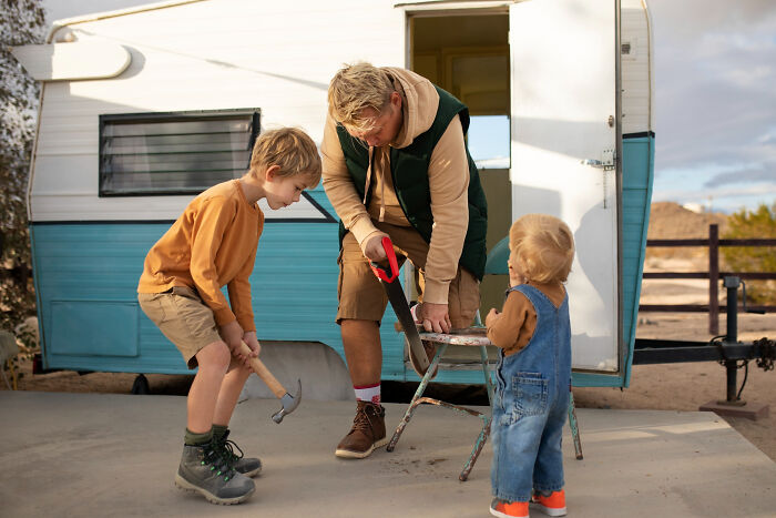 Father and children working with tools outside a camper, evoking childhood memories that felt sweet but now seem unsettling.