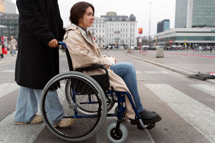 Young woman in wheelchair being pushed across city street, reflecting on childhood memories that felt sweet back then.