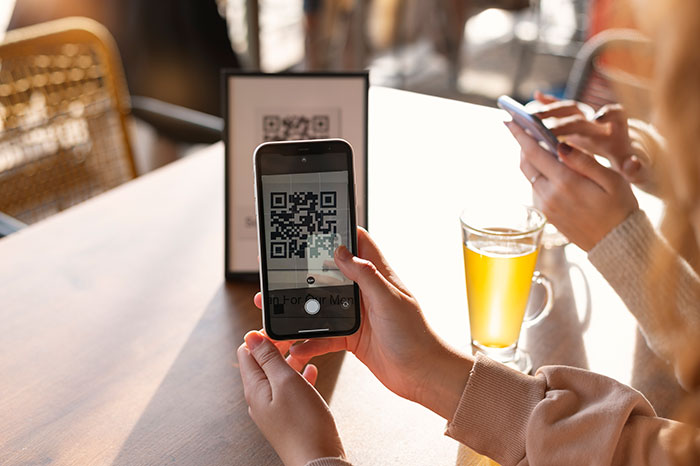 Person scanning a QR code with a smartphone while sitting at a table with a glass of tea, discussing hot take opinions.