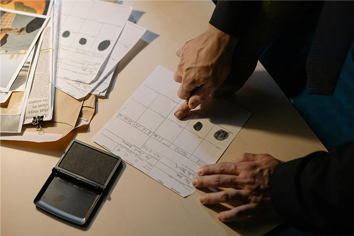 Person pressing finger on paper for fingerprinting in an office setting, illustrating pseudoscience and scam concepts.