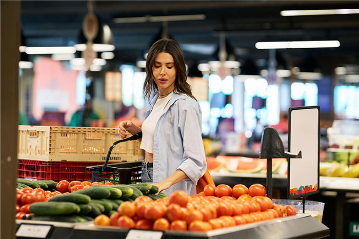 Woman shopping for fresh produce in a market, surrounded by tomatoes and cucumbers, highlighting pseudoscience and scams.