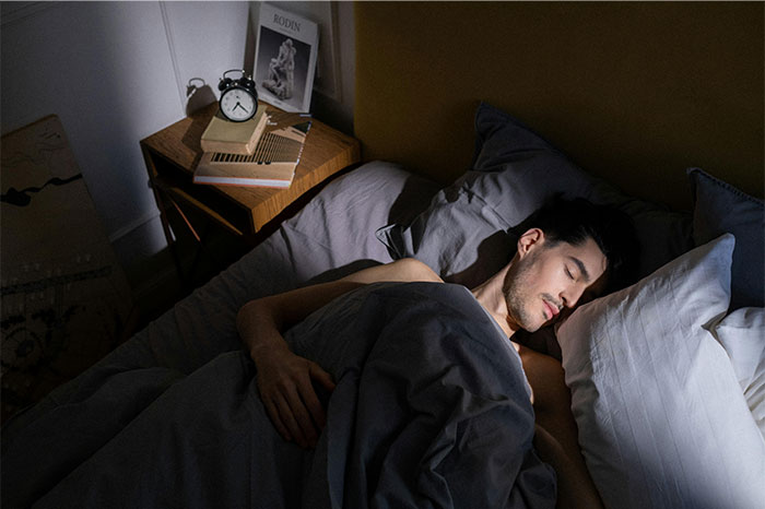 Man sleeping peacefully in bed with an alarm clock on the nightstand, illustrating pseudoscience and scams concept.